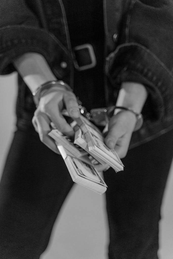 Grayscale image of handcuffed hands holding bundles of cash, emphasizing financial crime.